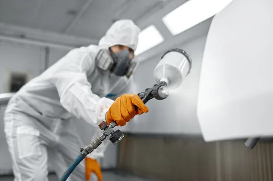 Painter in protective gear spraying a smooth finish in a spray booth